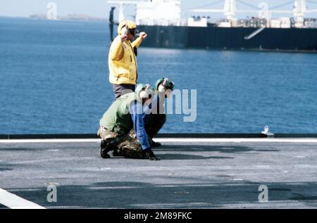 Due equipaggi del ponte di volo Marine sono in piedi mentre il direttore dell'aereo a bordo della nave logistica aerea USNS WRIGHT (T-AVB 3) segnala ad un elicottero entrante durante l'esercizio OCEAN VENTURE '88. La costa portoricana e la nave marittima di preposizionamento 2nd LT. GIOVANNI P. BOBO (T-AK 3007) sono sullo sfondo. Oggetto/Serie: OCEAN VENTURE '88 Paese: Mar dei Caraibi Foto Stock