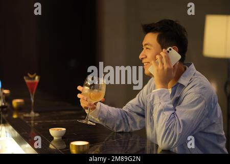 Felice giovane asiatico allegro al telefono al bar di notte. vista laterale Foto Stock