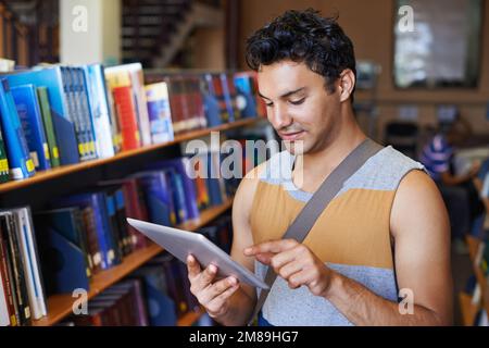 Controllare l'elenco del materiale di studio sul tablet digitale. Un bel giovane studente che lavora sul suo tablet digitale in biblioteca. Foto Stock