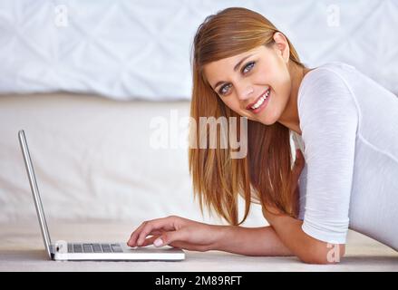 Shes sempre connessi. Ritratto di una giovane donna attraente che usa un computer portatile mentre sdraiata sul pavimento nella sua camera da letto. Foto Stock