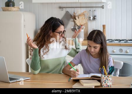 Ragazza teenage messa a fuoco ottimista con la bambina di studio scuola di studio della donna si siede al tavolo della cucina Foto Stock