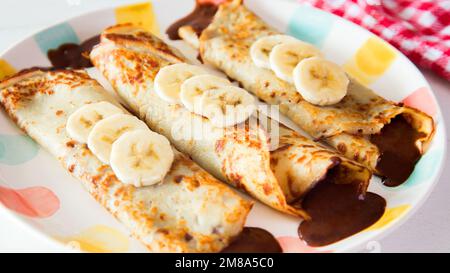 Crepes al cioccolato alla banana. Le crepes sono una ricetta di origine francese in cui viene preparato un impasto a base di farina, uova, latte, burro e sale. Foto Stock