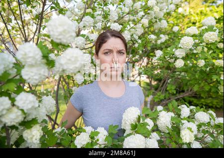 Donna infelice con un chiodo di garofano sul naso in una passeggiata in un parco fiorente. Foto Stock