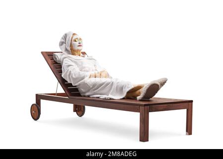 Donna matura in un accappatoio e capelli avvolti in un asciugamano posando con una maschera facciale e cetrioli sugli occhi isolati su sfondo bianco Foto Stock