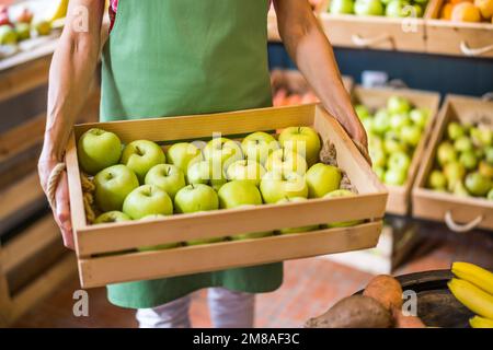 Lavoratore in frutta e verdura negozio è cestino con mele. Foto Stock