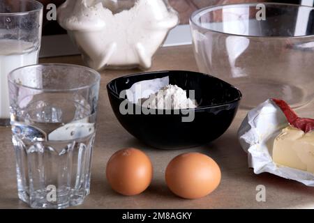 ciotola in vetro fotografico, uova, olio, farina, latte sul tavolo per preparare frittelle sottili Foto Stock