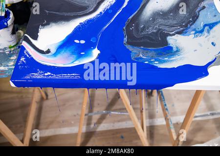 Vista dall'alto di tela bianca con immagine astratta di diversi colori bianco, blu, nero, grigio sulla scrivania con gambe in legno. Foto Stock
