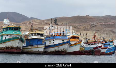 Barche da pesca ormeggiate nella baia di Pucusana con il paesaggio costiero deserto sullo sfondo. Pucusana, Lima, Perù Foto Stock