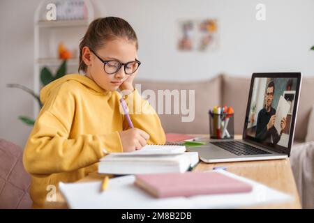 Ragazza stanca in occhiali che hanno lezioni online con tutor personale sul laptop. Il capretto si annoiava dallo studio, dall'esercitazione di matematica di scrittura nel taccuino. Vista laterale. ELearning e la scuola remota durante la quarantena di covid Foto Stock