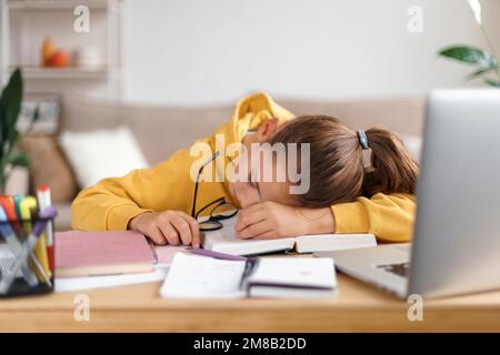 La ragazza della scuola esaurita che dorme alla scrivania mentre fa i lotti del lavoro, ottenendo pronta prima degli esami, sollecitata, è stata stanca dallo studiare, troppo imparare. Interni domestici. Homeschooling, formazione di distanza Foto Stock