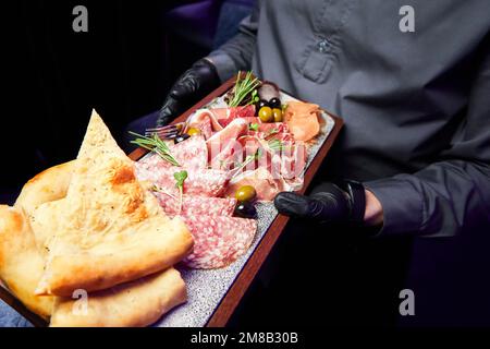 Il cameriere tiene un piatto di legno con varie prelibatezze secche a fette Foto Stock
