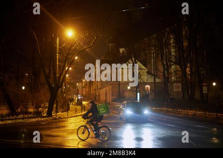 Corriere di bolt food su una bicicletta in un incrocio notturno di Cracovia, Polonia. Foto Stock