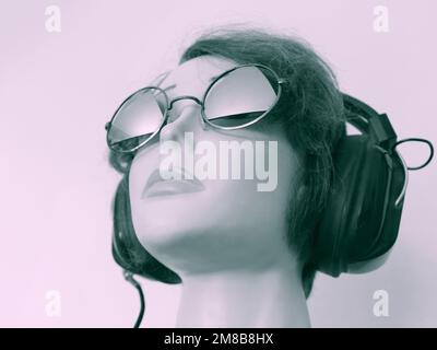 Ragazza manichino per capelli che ascolta musica attraverso l'ascolto di cuffie vintage, indossando occhiali da sole vintage. Foto Stock