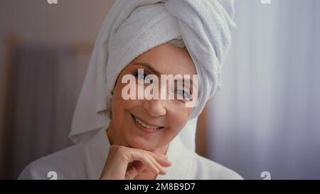 Headshot femmina ritratto felice 50s donna di mezza età 60s donna matura toccare la pelle del viso guardando la fotocamera con sorriso toccare viso indossarsi coccolare Foto Stock