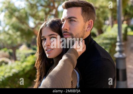 Giovane donna in maglione che tocca la barba del ragazzo su sfondo sfocato del parco il giorno di San Valentino Foto Stock