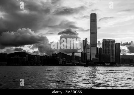 Il sole sorge su Kowloon, Hong Kong. Mare in primo piano. Edifici in silhouette. In bianco e nero. Foto Stock