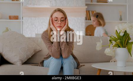 Stanco sconvolto madre caucasica seduta sul divano a casa triste frustrato stressato stressato stanchezza mamma soffrono mal di testa con rumore attivo difficile bambino Foto Stock