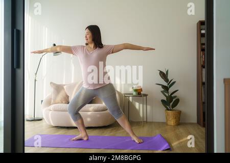 Intera lunghezza sana 6 mesi incinta calma donna asiatica meditare o fare esercizio di yoga a casa. Relax e stretching. Foto Stock
