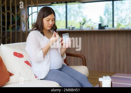 Donna asiatica madre incinta in possesso di farmaci integratori e bicchiere d'acqua - prendendo vitamine durante la gravidanza Foto Stock