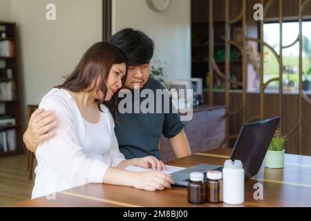 Il marito asiatico stava confortando la moglie incinta, che è stata rattristata dai risultati delle consultazioni in linea con i medici sul suo laptop nel soggiorno Foto Stock