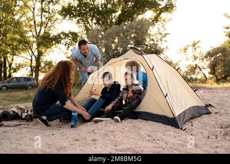 Famiglia che interagisce fuori dalla tenda al campeggio. felice grande famiglia campeggio al tramonto. Goditi il tempo con la famiglia. Viaggi, avventure, vacanze con bambini con Foto Stock