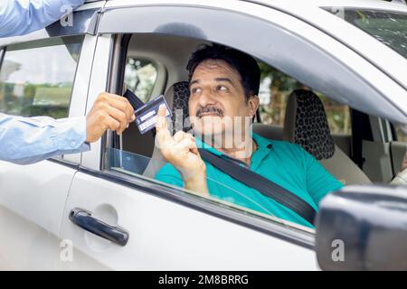 Uomo maturo indiano felice seduto in auto che indossa la cintura di sicurezza dare carta di credito o di debito per riempire la benzina in auto presso la stazione di servizio. Pagamento senza contanti. Foto Stock