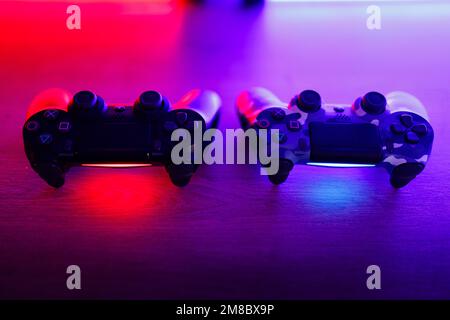 Due gamepad su un tavolo di legno con retroilluminazione rossa e blu. Foto Stock