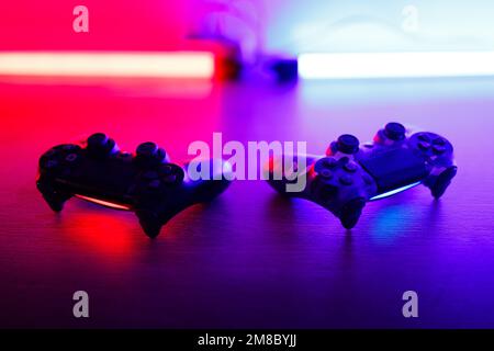 Due gamepad su un tavolo di legno con retroilluminazione rossa e blu. Foto Stock