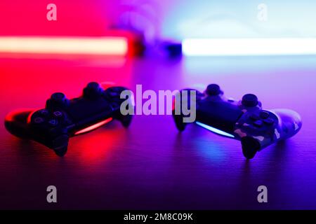 Due gamepad su un tavolo di legno con retroilluminazione rossa e blu. Foto Stock