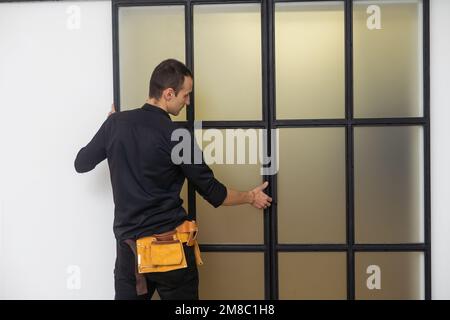 Un bel giovane uomo che installa la doppia porta scorrevole del patio dentro un nuovo cantiere Foto Stock