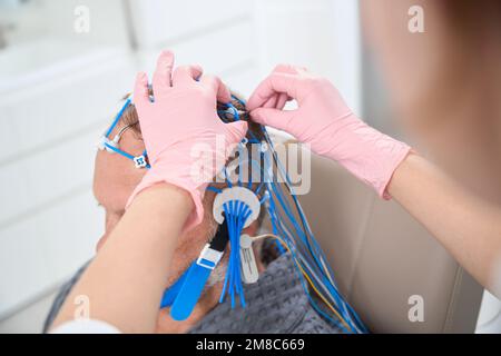 L'operatore sanitario rimuove gli elettrodi dalla testa del paziente Foto Stock