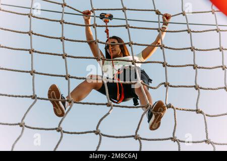 Giovane arrampicatore che ha difficoltà a pendere sulla parete di corde nel parco avventura Foto Stock