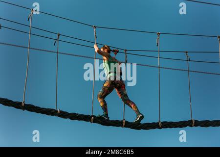 Donna adulta esperta che corre attraverso il difficile percorso nel parco avventura con facilità Foto Stock