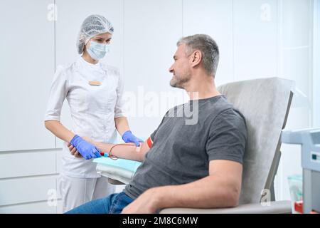 L'operatore sanitario in abiti medici prende campione di sangue dall'uomo Foto Stock