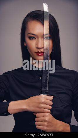 Ritratto, spada e guerriero con una donna asiatica in studio su sfondo grigio per arti marziali o combattimento. Allenamento, fantasia e arma con un ninja Foto Stock