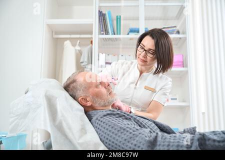 Un uomo anziano piacevole riceve iniezioni di collagene in clinica di medicina estetica Foto Stock