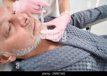 L'uomo dai capelli grigi riceve iniezioni di bellezza in una clinica di medicina estetica Foto Stock