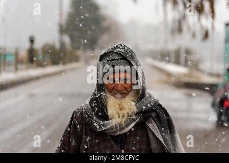 Un uomo anziano guarda mentre cammina in mezzo alla nevicata. Il Kashmir ha ricevuto nevicate fresche, con le cali più alte della valle che hanno ricevuto nevicate da moderate a pesanti e nevicate da leggere a moderate in pianura, causando una visibilità distruttiva. Questo ha influito sulle operazioni di volo insieme alla chiusura dell'autostrada nazionale Srinagar-Jammu. Foto Stock