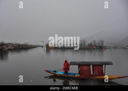 Un uomo che indossa un impermeabile rema la sua barca sul lago dal durante le nevicate. Parti della valle di Kashmir compreso Srinagar ha ricevuto nevicate che portano alla chiusura della vitale Srinagar-Jammu autostrada nazionale e la cancellazione delle operazioni di volo, funzionari qui ha detto. Foto Stock