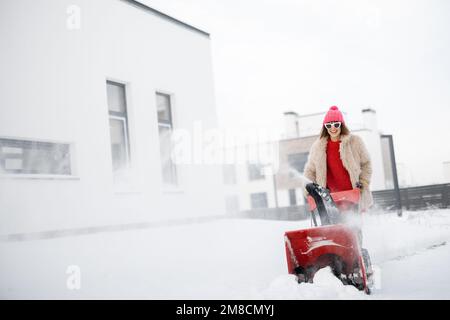 Donna rimuove la neve con un lancianeve vicino casa Foto Stock