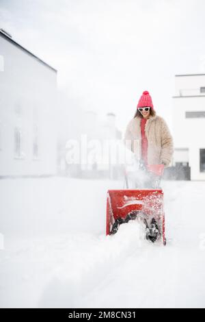 Donna rimuove la neve con un lancianeve vicino casa Foto Stock