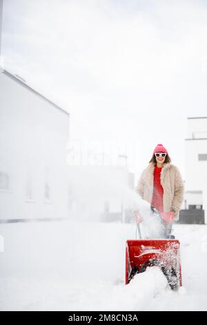 Donna rimuove la neve con un lancianeve vicino casa Foto Stock