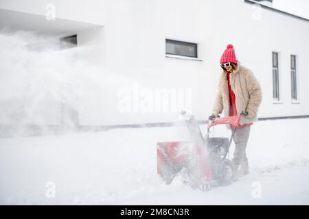 Donna rimuove la neve con un lancianeve vicino casa Foto Stock