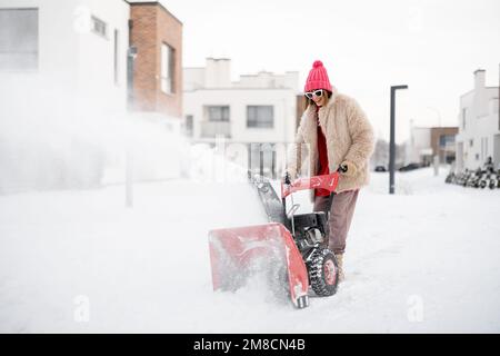 Donna rimuove la neve con un lancianeve vicino casa Foto Stock