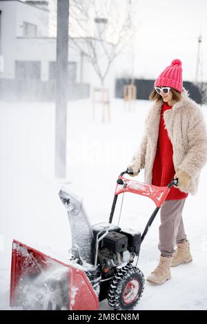Donna rimuove la neve dal percorso con una macchina spazzaneve Foto Stock