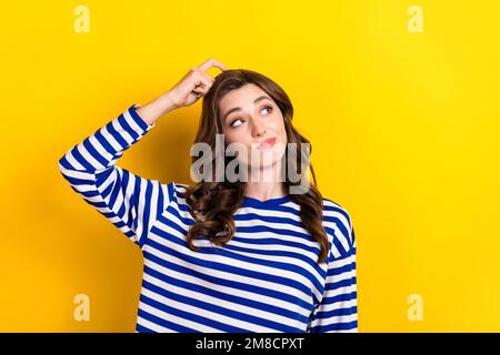 Foto di attraente giovane donna gratta testa guardare interessato spazio vuoto vestito elegante vestito a righe isolato su sfondo giallo Foto Stock