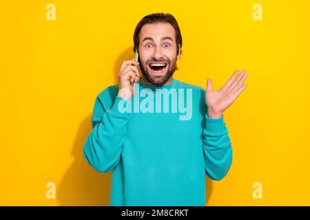 Foto di impressionato funky ragazzo vestito teal vestito comunicante mela samsung moderno gadget isolato sfondo di colore giallo Foto Stock