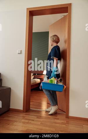 Cameriera in uniforme per la pulizia della cassetta porta appartamenti con detersivi e stracci Foto Stock