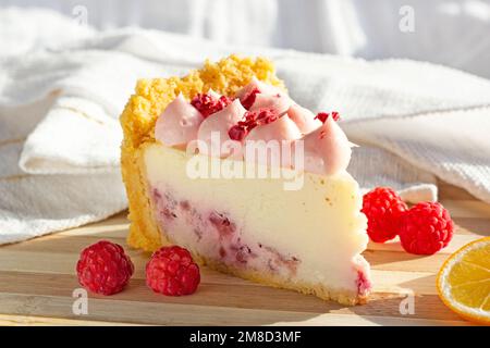 Deliziosa fetta di formaggio lampone dolce bianco e rosa con bacche fresche sul bordo di legno in cucina. Foto Stock