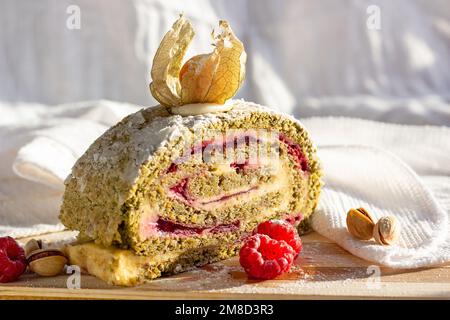 Involtini di meringa al pistacchio verde con marmellata di lamponi su fondo in legno chiaro in cucina. Foto Stock